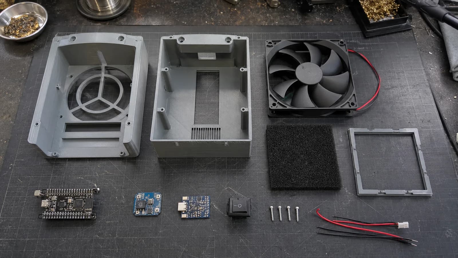 Quạt máy tính 120 mm, tấm lọc carbon, ESP32-C3, mạch điều khiển và các chi tiết vỏ in 3D được đặt trên bàn.