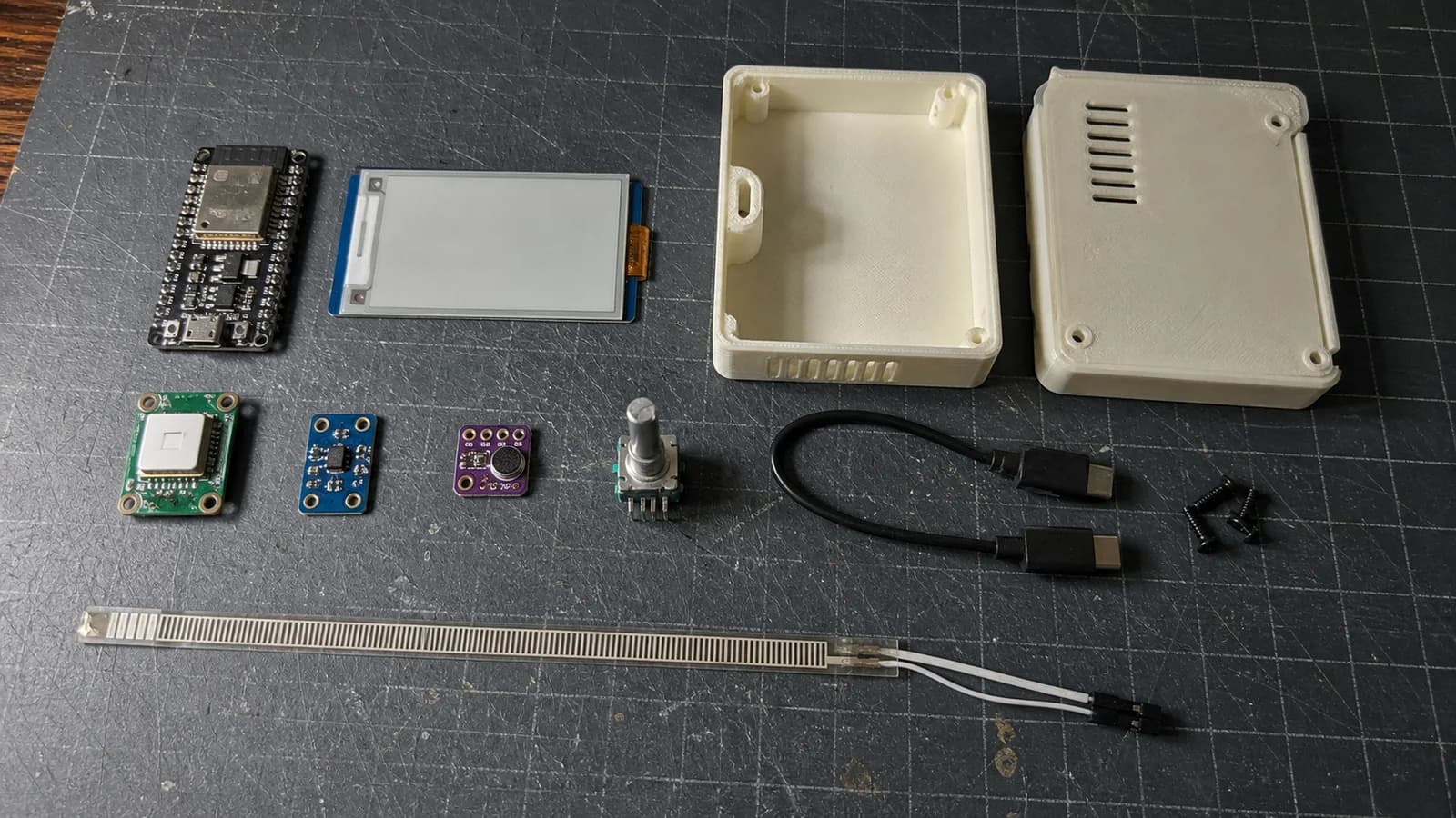 ESP32-S3, màn hình e-paper, cảm biến SCD41, cảm biến ánh sáng, microphone MEMS, encoder và vỏ đồng hồ in 3D đặt trên bàn.