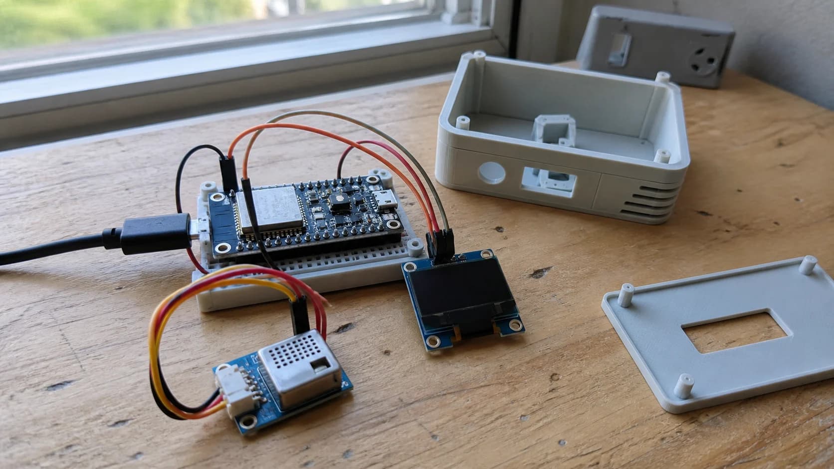 Prototype thiết bị nhắc mở cửa sổ gồm board ESP32, cảm biến CO2 SCD40 hoặc SCD41, màn hình OLED và vỏ in 3D đặt trên bàn gần cửa sổ.